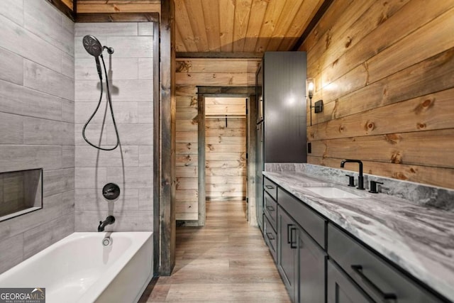 bathroom featuring wood ceiling, wooden walls, wood-type flooring, tiled shower / bath, and vanity