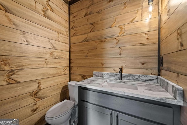 bathroom featuring vanity, toilet, and wood walls