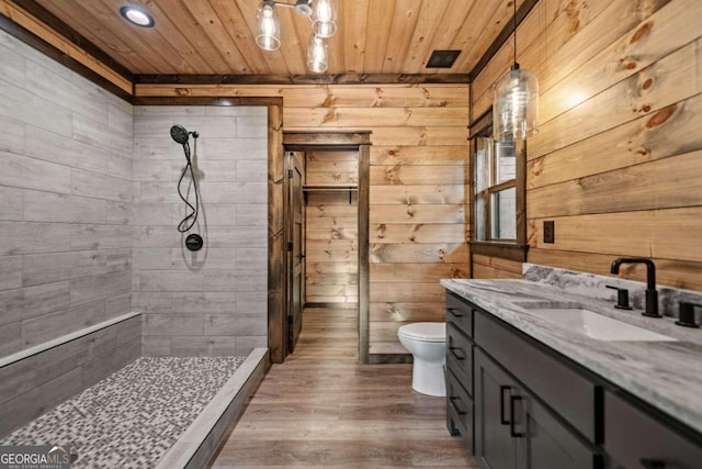 bathroom with vanity, tiled shower, toilet, and wood walls