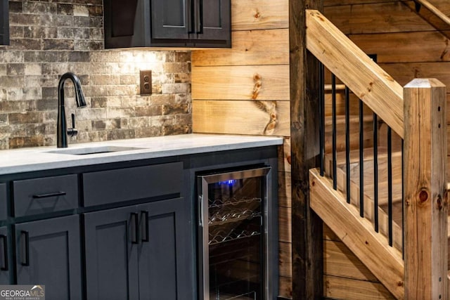 bar featuring wood walls, tasteful backsplash, sink, and beverage cooler