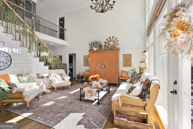 living room featuring a notable chandelier, wood walls, a towering ceiling, and dark wood-type flooring