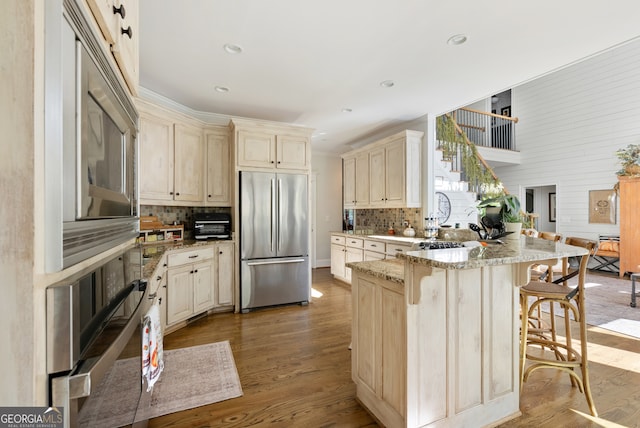 kitchen featuring hardwood / wood-style floors, backsplash, built in appliances, light stone countertops, and a kitchen bar