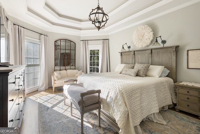 bedroom featuring hardwood / wood-style floors, a notable chandelier, ornamental molding, and a tray ceiling