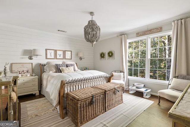 bedroom featuring crown molding, light hardwood / wood-style flooring, wooden walls, and an inviting chandelier