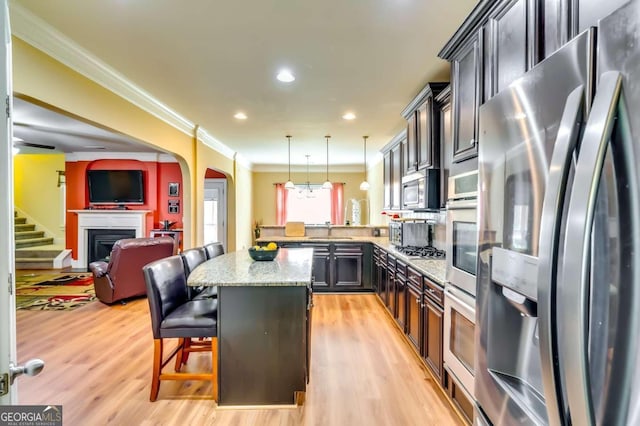 kitchen featuring appliances with stainless steel finishes, a center island, decorative light fixtures, light stone counters, and a breakfast bar