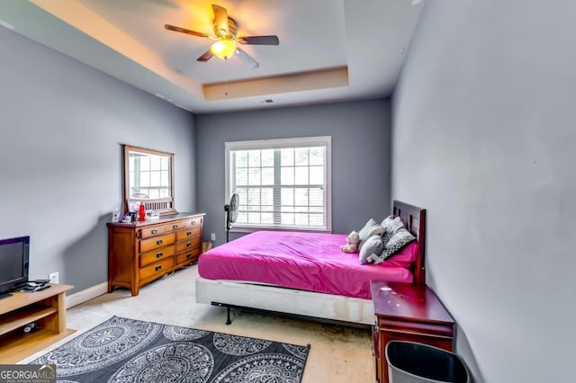 bedroom featuring light carpet, a tray ceiling, and ceiling fan