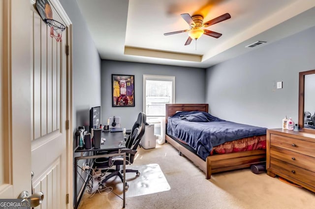 carpeted bedroom with ceiling fan and a tray ceiling