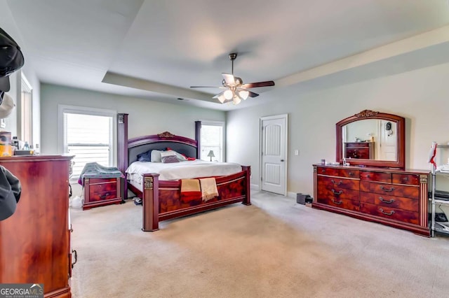 carpeted bedroom with a raised ceiling and ceiling fan