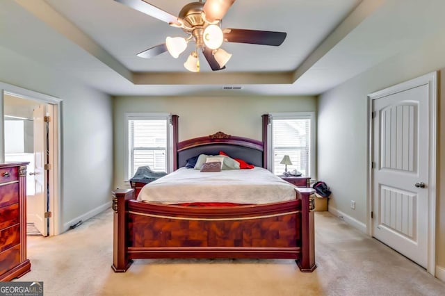 bedroom featuring a raised ceiling, light carpet, multiple windows, and ceiling fan