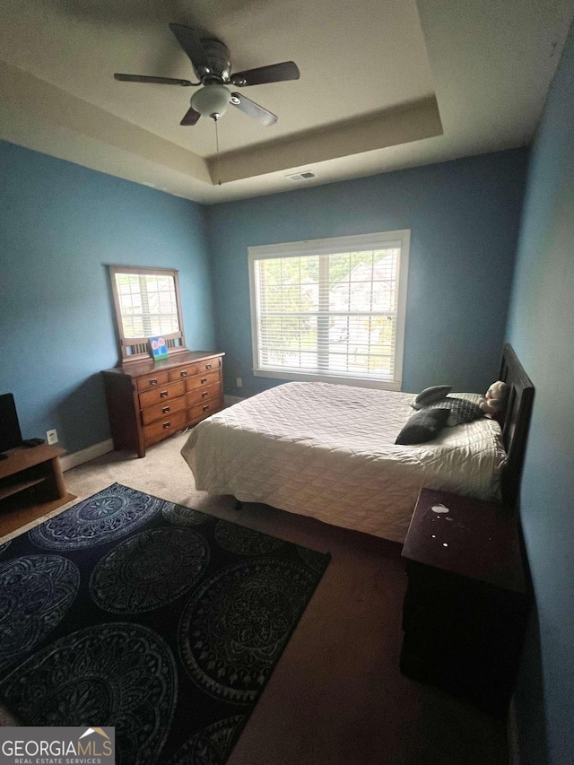 bedroom with ceiling fan, a tray ceiling, carpet, and multiple windows