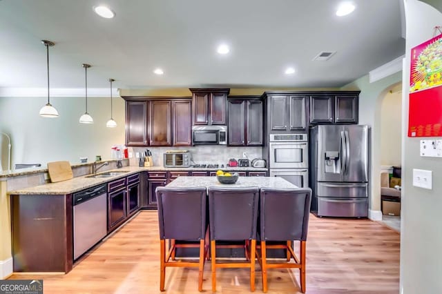 kitchen featuring hanging light fixtures, stainless steel appliances, kitchen peninsula, a kitchen bar, and light wood-type flooring