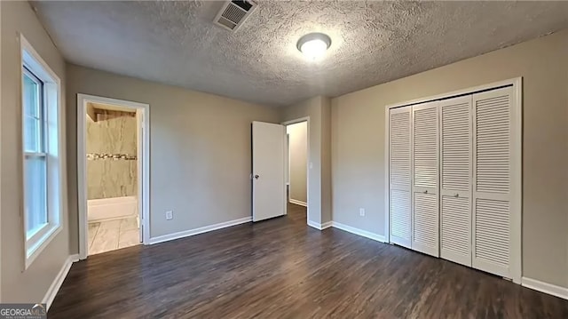 unfurnished bedroom with a closet, a textured ceiling, ensuite bath, and dark hardwood / wood-style flooring