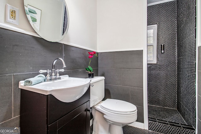 bathroom with a tile shower, vanity, tile patterned floors, toilet, and tile walls