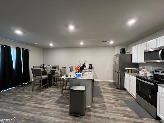 kitchen with white cabinetry, stainless steel appliances, dark wood-type flooring, a breakfast bar area, and a center island with sink