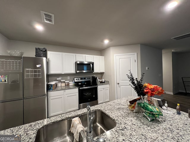 kitchen with light stone countertops, appliances with stainless steel finishes, sink, white cabinetry, and hardwood / wood-style flooring