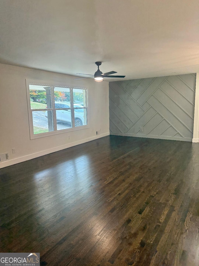 spare room featuring dark wood-type flooring, ceiling fan, and wood walls