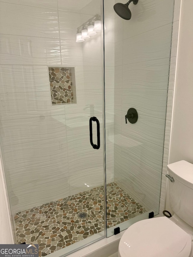 bathroom featuring a shower with door and toilet