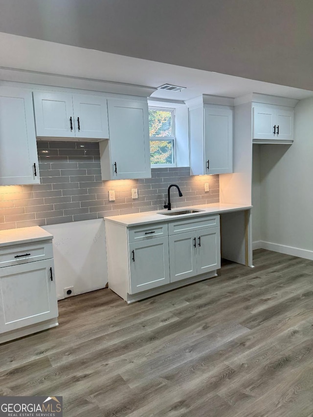 kitchen with light hardwood / wood-style flooring, white cabinets, tasteful backsplash, and sink