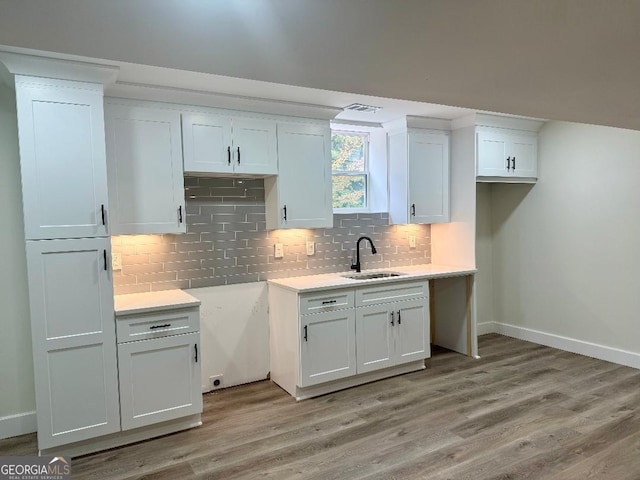 kitchen with baseboards, a sink, decorative backsplash, and light wood-type flooring