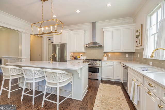 kitchen featuring premium appliances, sink, wall chimney exhaust hood, white cabinets, and a center island with sink