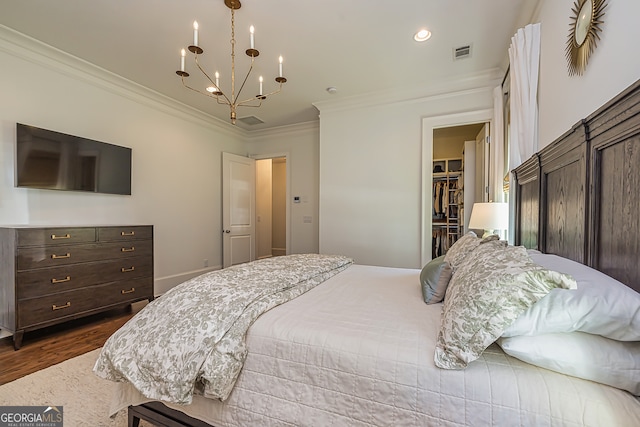 bedroom with a notable chandelier, a spacious closet, ornamental molding, dark wood-type flooring, and a closet