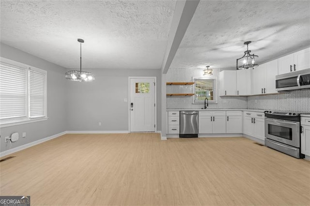 kitchen featuring backsplash, pendant lighting, white cabinetry, appliances with stainless steel finishes, and light hardwood / wood-style floors