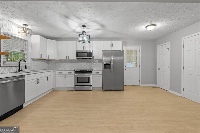 kitchen with sink, decorative light fixtures, light wood-type flooring, white cabinetry, and appliances with stainless steel finishes