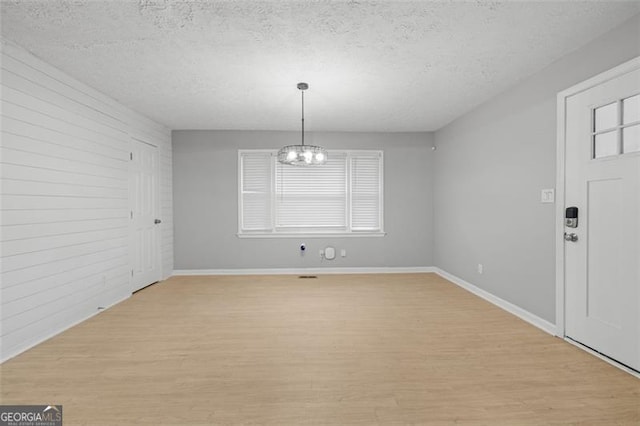 unfurnished dining area featuring light hardwood / wood-style floors, a textured ceiling, and a chandelier