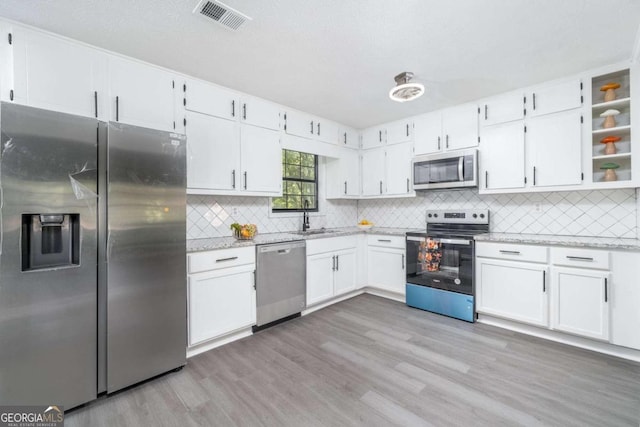 kitchen featuring light stone countertops, white cabinets, light hardwood / wood-style flooring, and stainless steel appliances