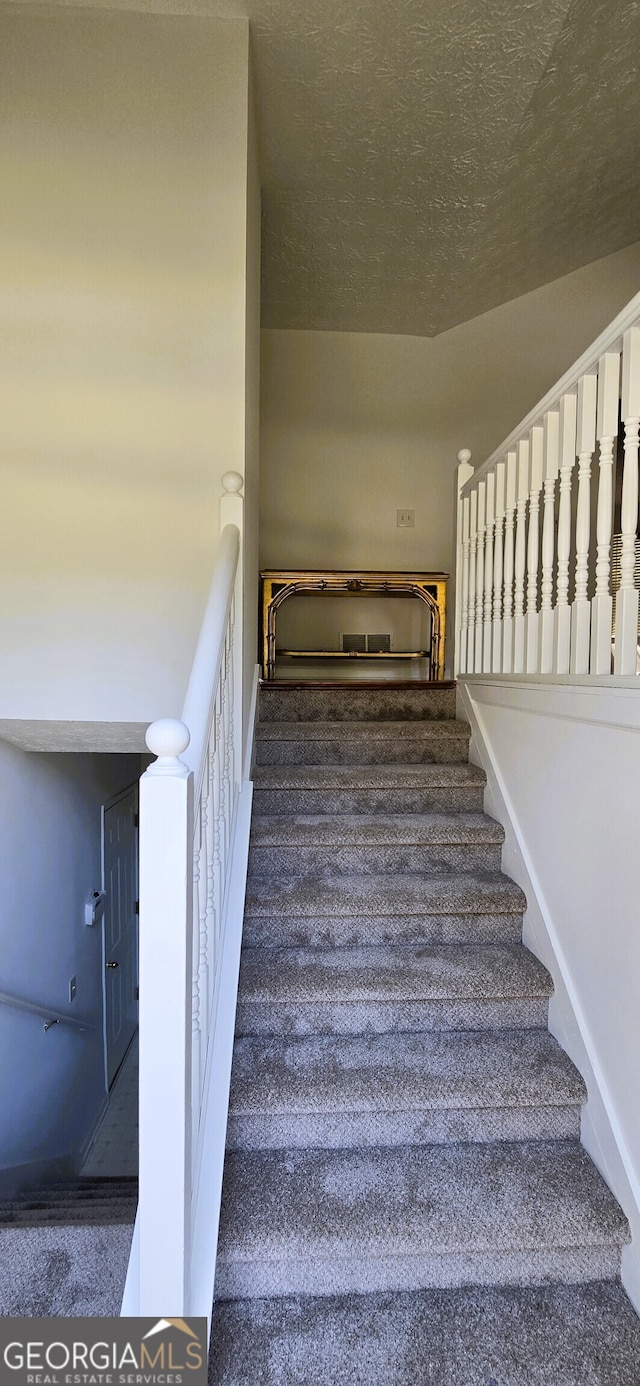 stairway with carpet flooring and a textured ceiling