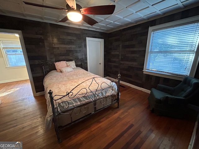 bedroom featuring dark wood-type flooring, ceiling fan, and wooden walls