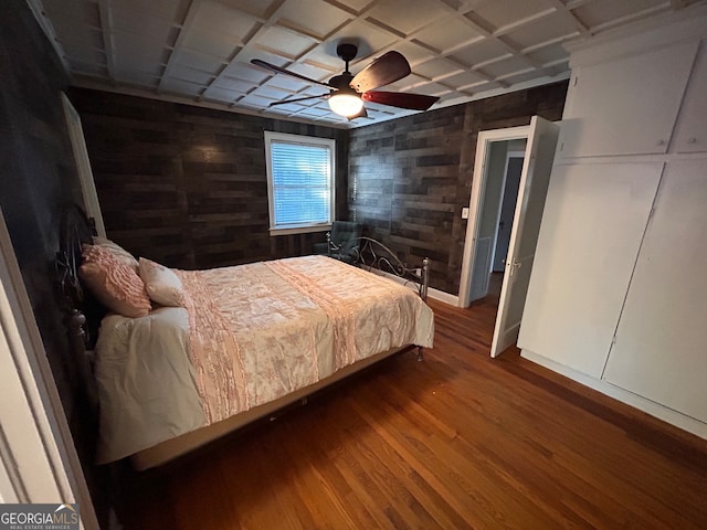 bedroom with wooden walls, wood-type flooring, and ceiling fan