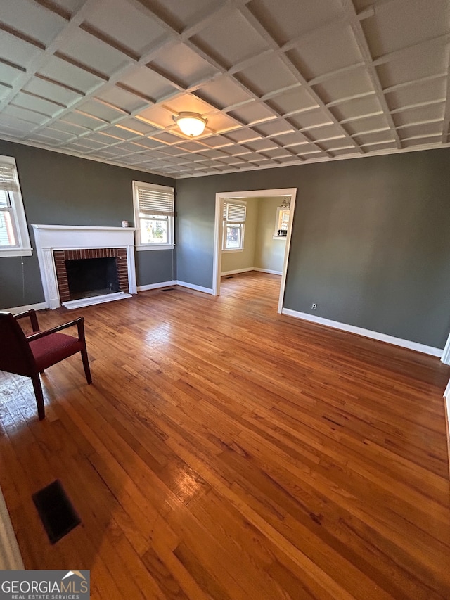 unfurnished living room featuring hardwood / wood-style floors, coffered ceiling, and a brick fireplace