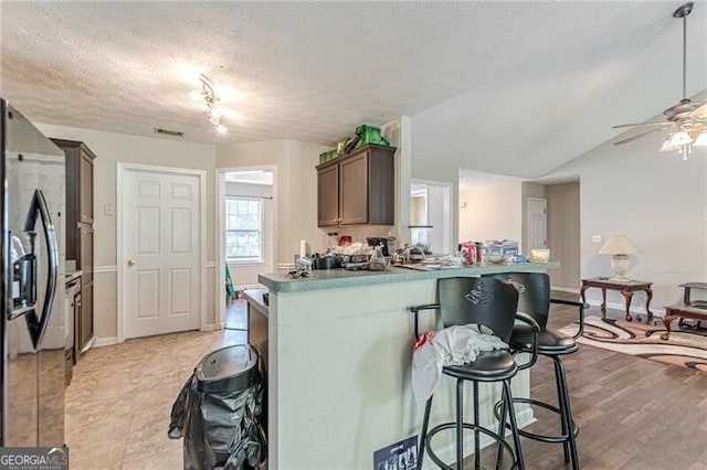 kitchen with a textured ceiling, a kitchen breakfast bar, ceiling fan, light hardwood / wood-style flooring, and stainless steel refrigerator with ice dispenser