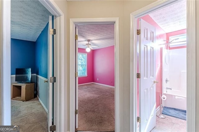 hall with a textured ceiling and light colored carpet