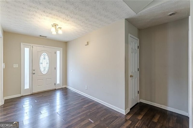 foyer entrance with dark wood-type flooring, a notable chandelier, and a textured ceiling