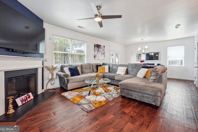 living room with dark wood-type flooring, a wealth of natural light, and ceiling fan with notable chandelier