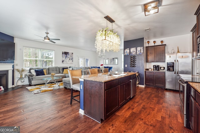 kitchen featuring appliances with stainless steel finishes, dark hardwood / wood-style flooring, a kitchen breakfast bar, and a kitchen island with sink