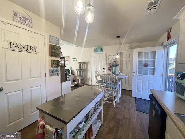 kitchen featuring black dishwasher, dark wood-type flooring, white cabinetry, and hanging light fixtures