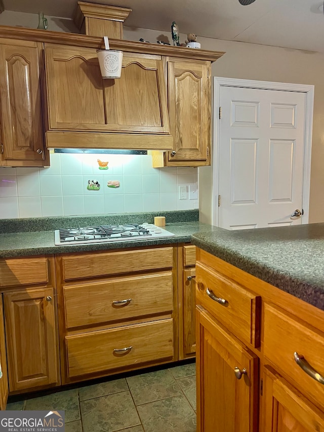 kitchen featuring backsplash, white gas stovetop, and dark tile patterned flooring