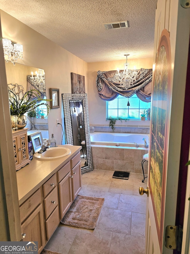 bathroom featuring vanity, a textured ceiling, tiled tub, and an inviting chandelier