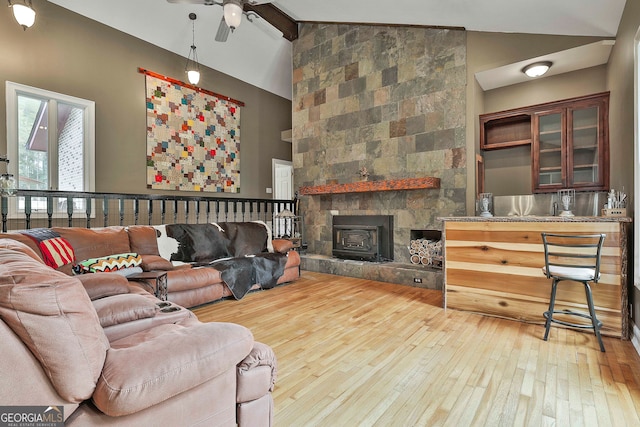 living room featuring beamed ceiling, wood-type flooring, a wood stove, and high vaulted ceiling