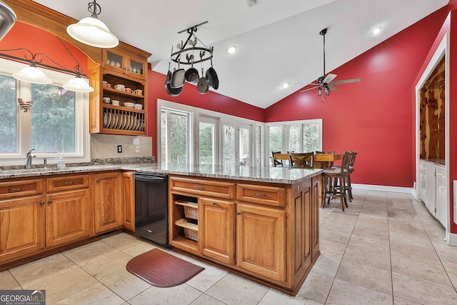 kitchen featuring ceiling fan with notable chandelier, light stone counters, black dishwasher, kitchen peninsula, and decorative light fixtures