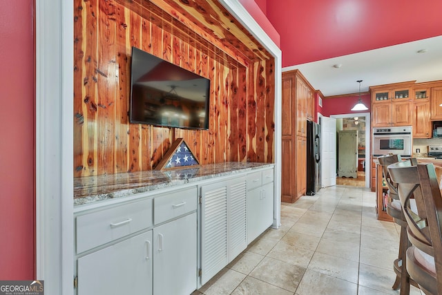 kitchen featuring stainless steel appliances, light tile patterned flooring, light stone countertops, hanging light fixtures, and wooden walls