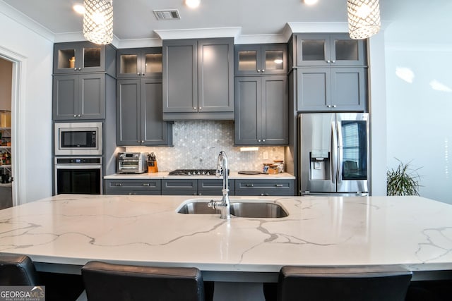 kitchen with appliances with stainless steel finishes, sink, hanging light fixtures, ornamental molding, and light stone counters