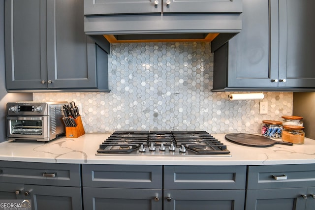 kitchen with extractor fan, stainless steel gas stovetop, gray cabinetry, decorative backsplash, and light stone countertops