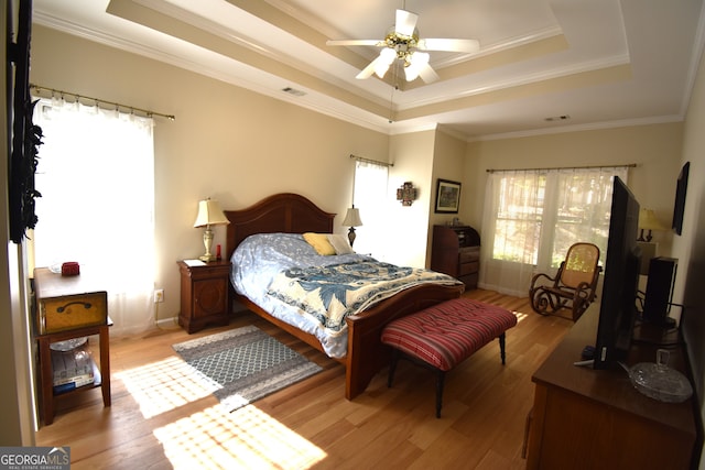 bedroom featuring ornamental molding, light hardwood / wood-style flooring, a tray ceiling, and ceiling fan