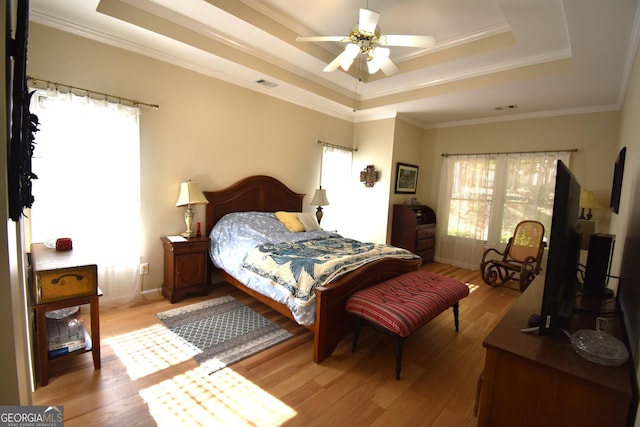 bedroom with ornamental molding, light hardwood / wood-style floors, and a tray ceiling