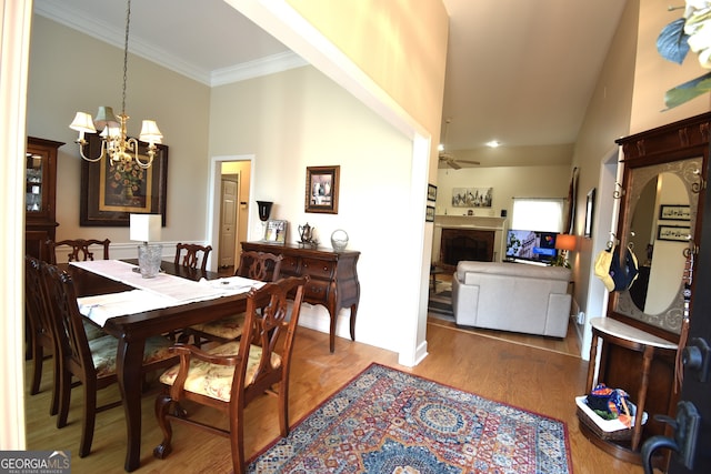 dining space with ornamental molding, ceiling fan with notable chandelier, wood-type flooring, and high vaulted ceiling