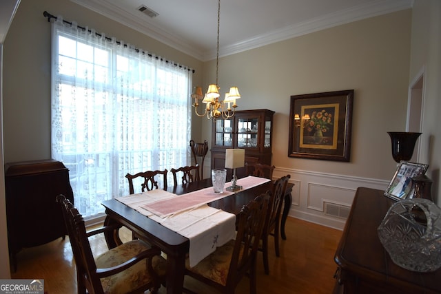 dining room with dark wood-type flooring, ornamental molding, and an inviting chandelier